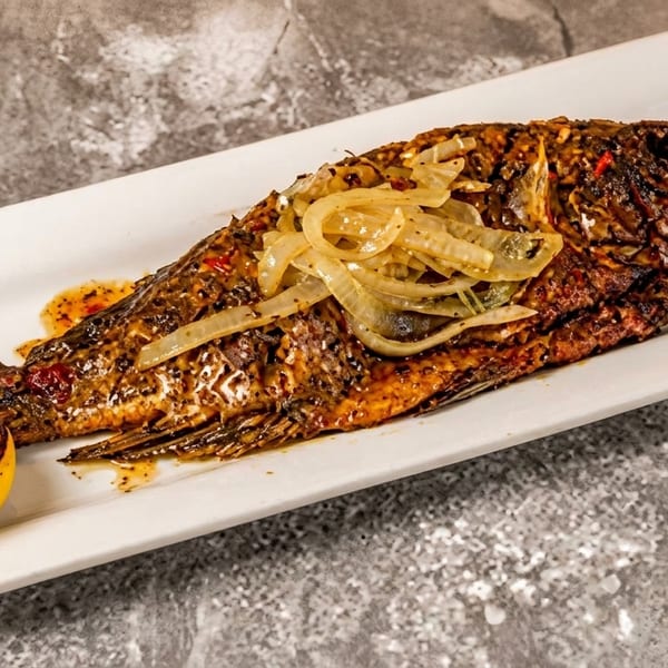 Whole grilled fish topped with caramelized onions, served with a charred lemon and cilantro.