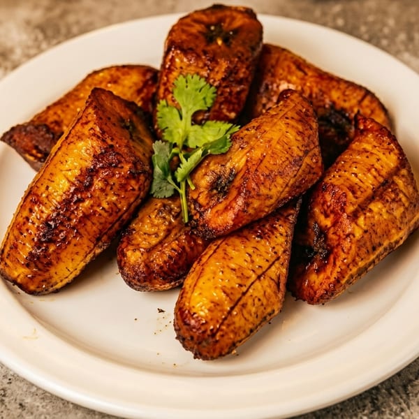 A white plate holds several golden-brown fried plantains, garnished with a sprig of cilantro.