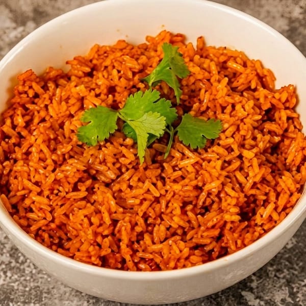 A white bowl filled with vibrant orange jollof rice, garnished with fresh green cilantro.