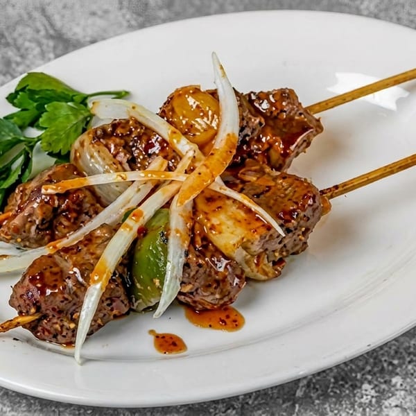Two skewers of grilled meat and vegetables, topped with sliced onions and sauce, on a white plate.