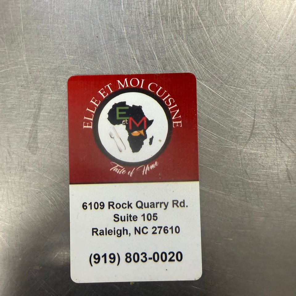 Restaurant sign for Eet Moi Cuisine featuring an African map logo, address, and phone number on a scratched metal surface.