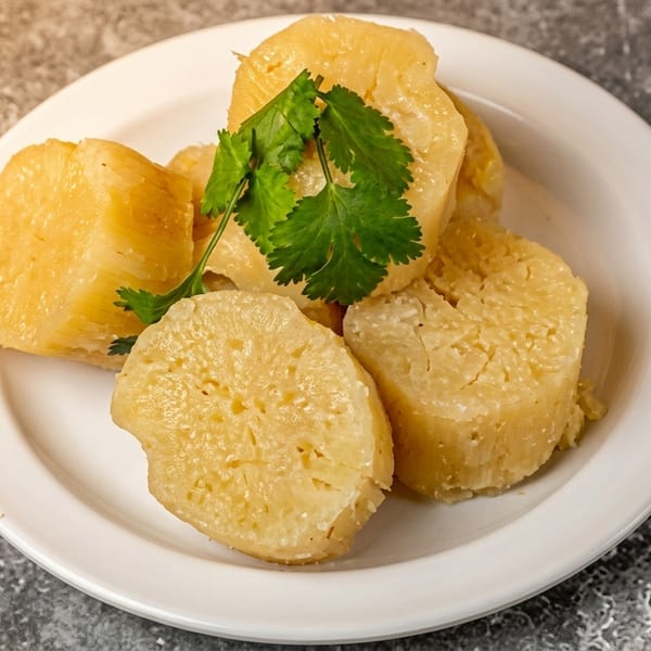 Boiled cassava pieces, garnished with fresh cilantro, served on a white plate.